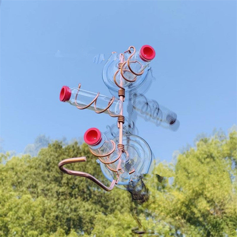 Clear glass hummingbird feeder with spiral metal accents and red openings, set against a bright blue sky and green trees.