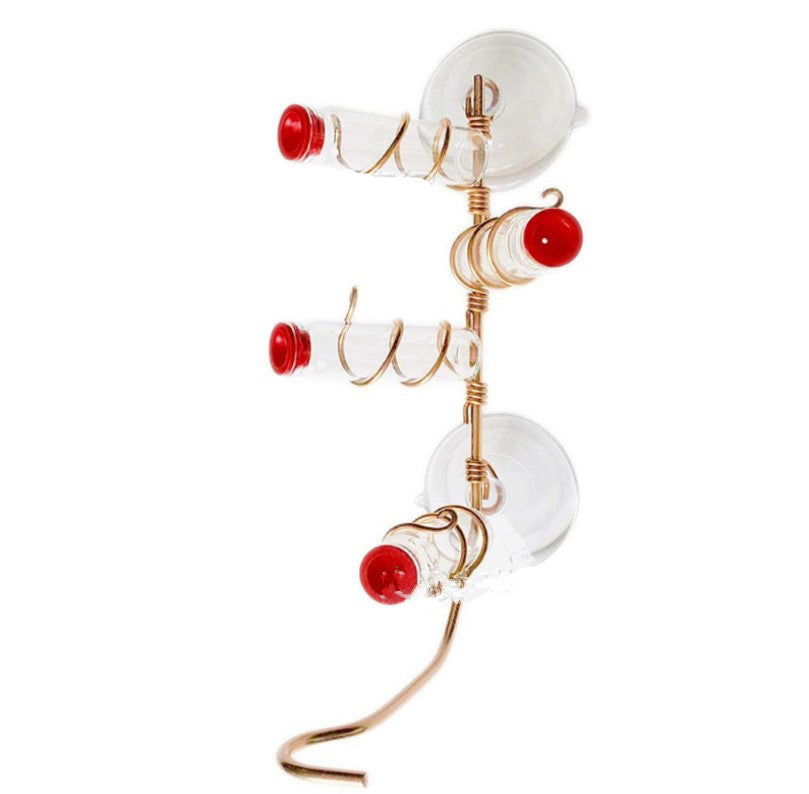 Glass bird feeder with three spiral perches and red caps, mounted on a vertical support with suction cups. Designed for window attachment, featuring a gold metal frame.