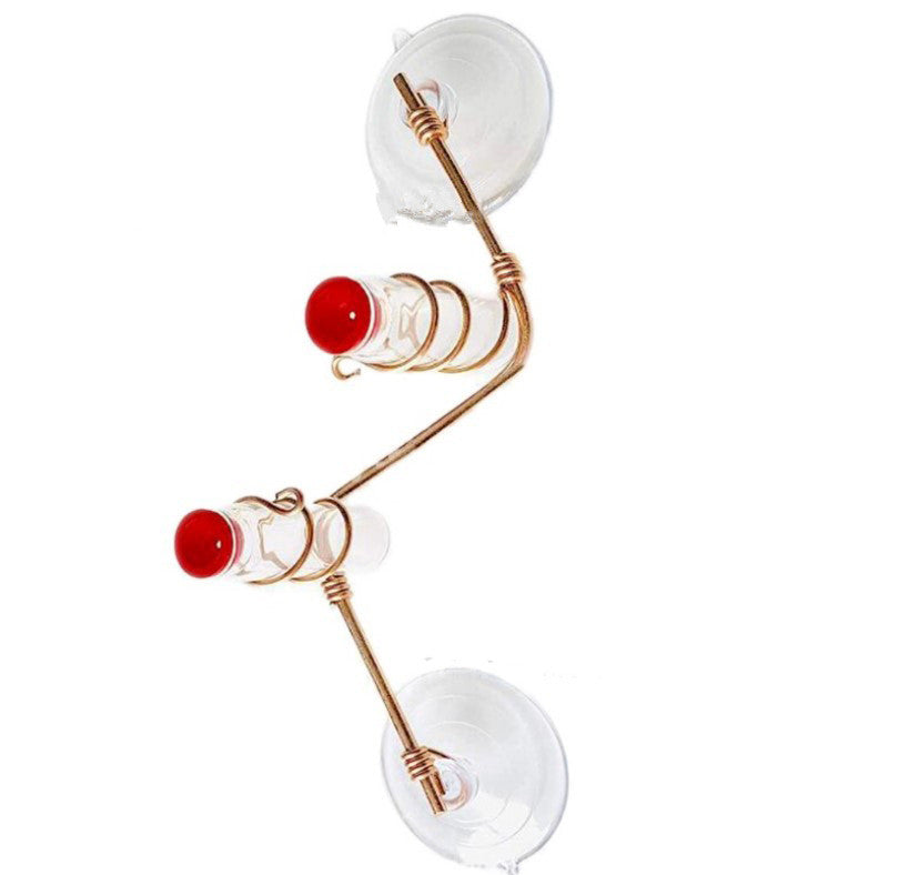 A brass bird feeder with two suction cups for window attachment, featuring two small glass containers, each capped with a red lid and accented with star designs.