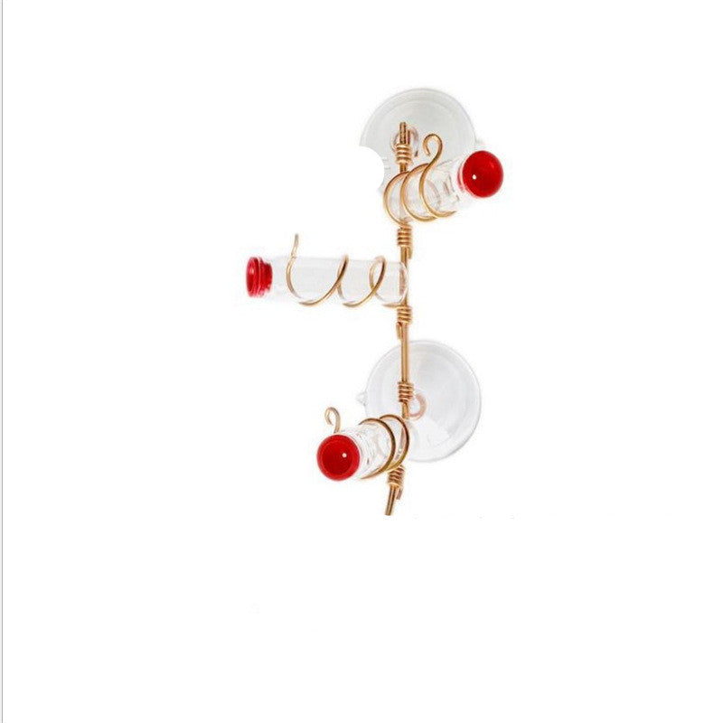 Two transparent suction cups with gold wire spirals hold glass tubes with red ends. The hanging holder creates a minimalist, decorative wall organizer against a white background.