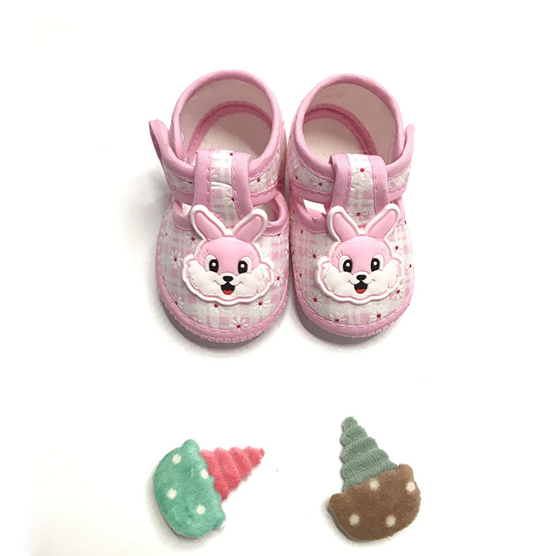 Pink baby shoes with bunny faces on the front, set against a white background. Below are two multi-colored plush ice cream cones with polka dots.