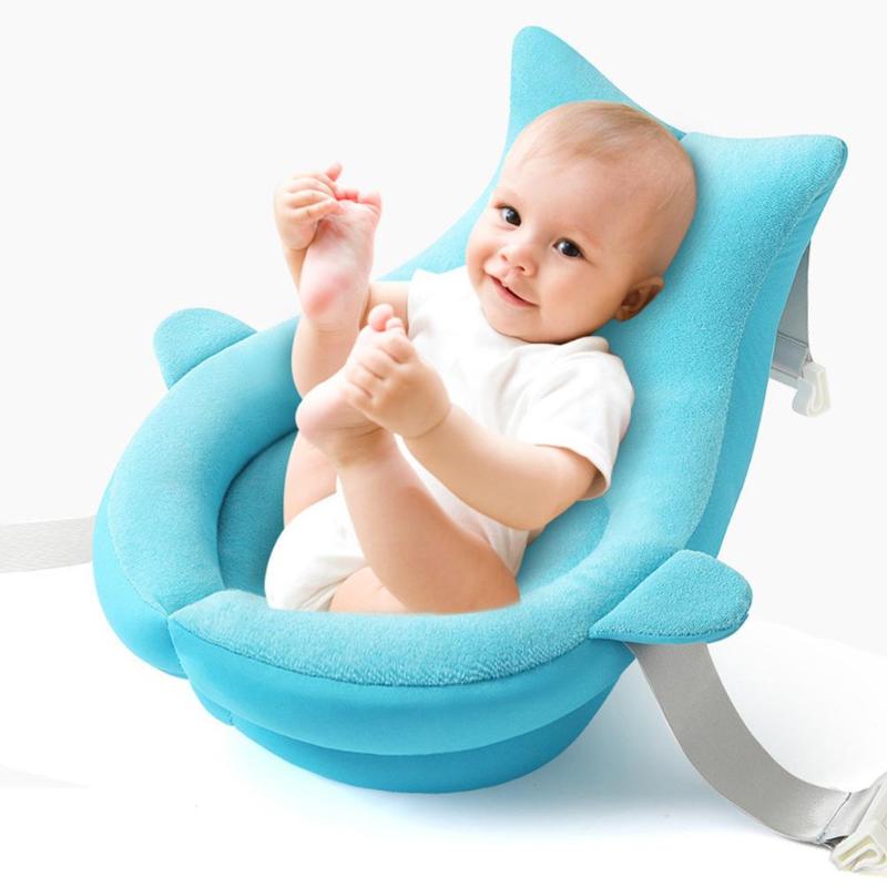 A happy baby in a white onesie sits in a plush, blue baby seat, smiling and holding their feet. The seat has a comfortable, ergonomic design with side supports.