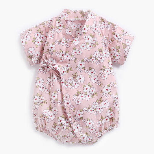 Pink floral baby romper with short sleeves and wrap closure, featuring a white and green flower pattern and snap buttons at the bottom.