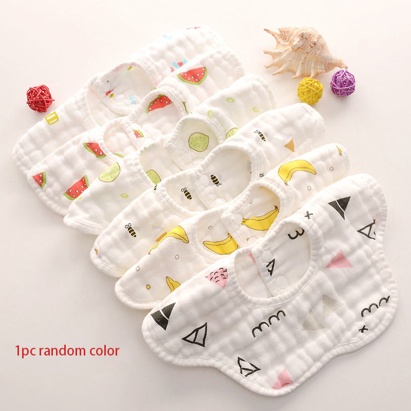 Seven baby bibs with various colorful patterns, including fruit and geometric shapes, displayed in a row. Nearby are a shell and colorful decorative balls.
