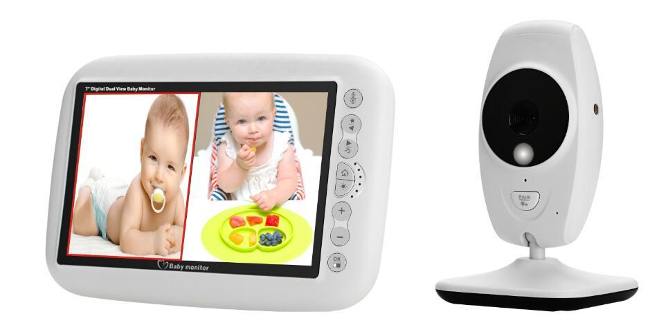 Baby monitor with a large display screen showing two images of a baby: one lying down with a pacifier and another eating from a colorful plate. The camera is positioned upright beside it.