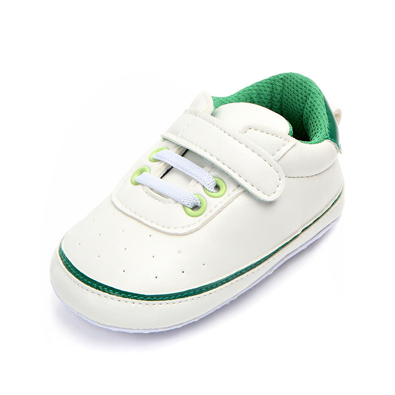 White baby sneaker with a green interior, green accents, and a velcro strap. Features include white laces through green eyelets and a perforated toe area for ventilation.