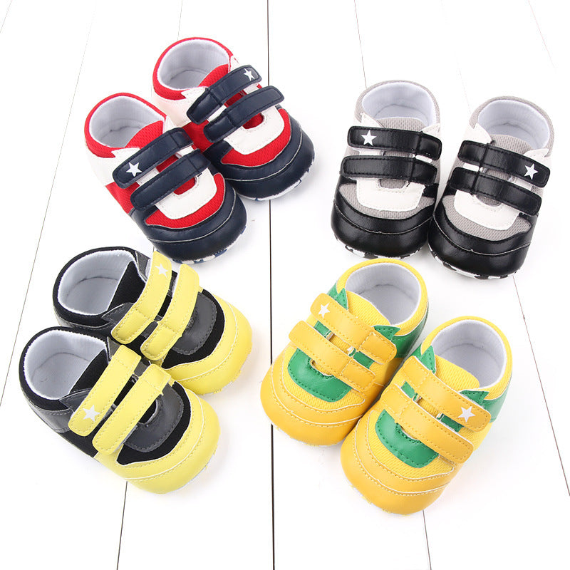 Colorful baby shoes arranged on a white wooden surface, featuring pairs in red, black, and yellow with double Velcro straps and star accents.