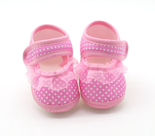 Pink baby shoes with white polka dots, featuring velcro straps and a frilly lace trim around the ankle, displayed on a plain white background.