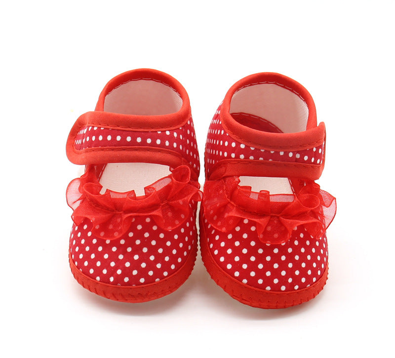 Red baby shoes with white polka dots and frilly bows, featuring a hook-and-loop strap, on a plain white background.