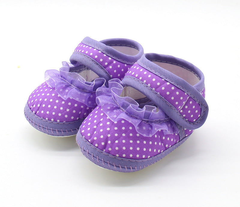 Purple baby shoes with white polka dots and Velcro straps. The shoes feature ruffled tulle accents on the top, and have a soft sole, suitable for infant wear.