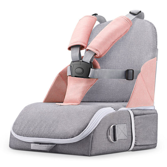 A portable baby booster seat in grey and pink fabric with adjustable safety straps, a cushioned seat, and a secure plastic buckle, designed for travel convenience.