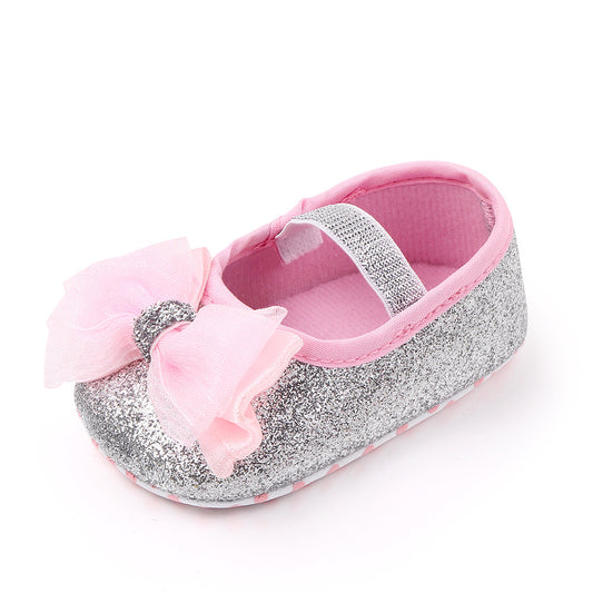 Silver glitter baby shoe with soft pink lining and a matching pink bow on top. It features a sparkly elastic strap for secure fit.