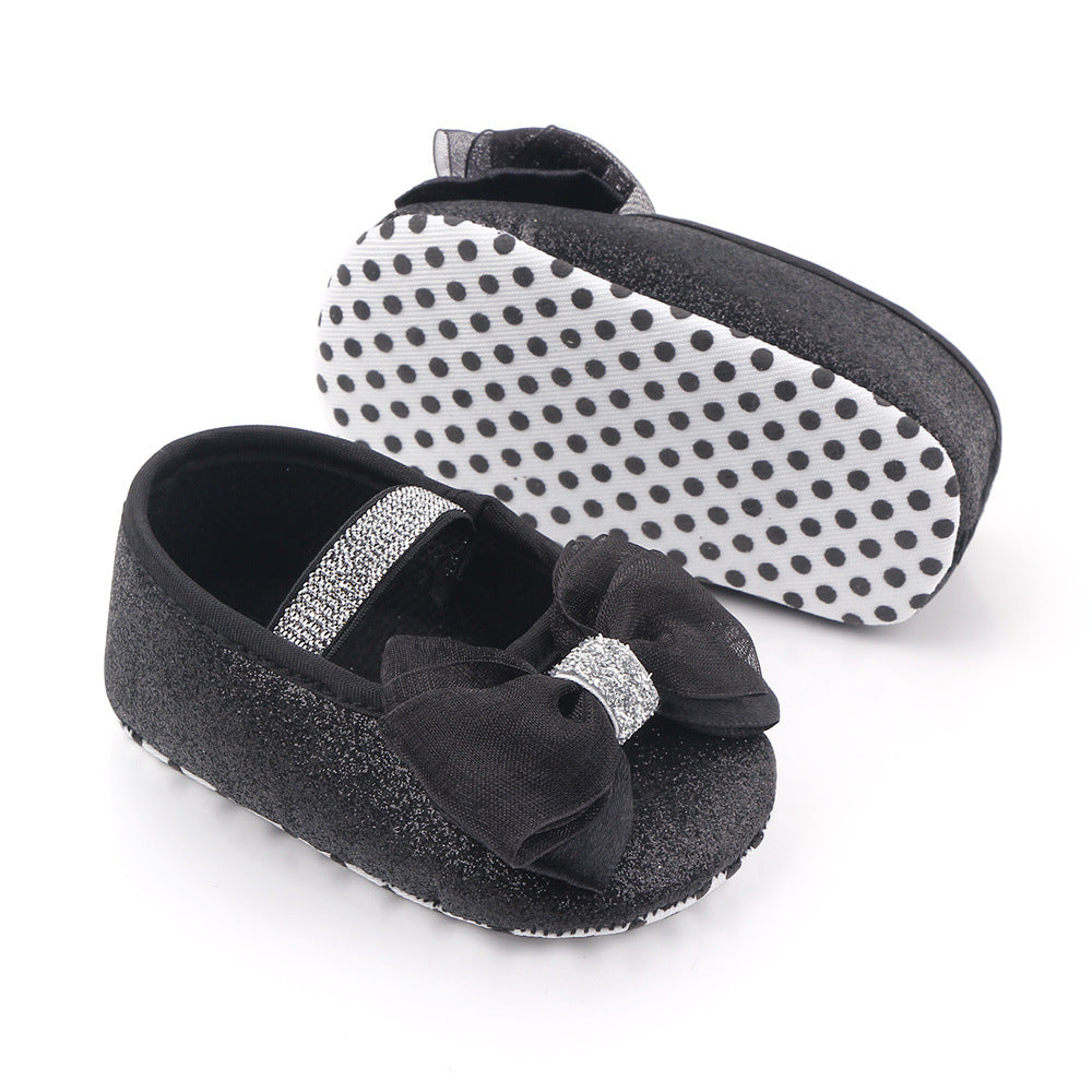Black baby shoes with glittery bow and strap, sparkle detail, and white polka dot soles.