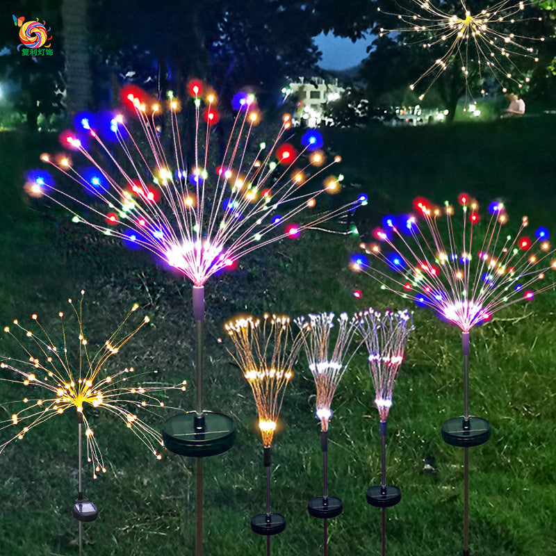 Colorful LED garden lights resembling fireworks, glowing in red, blue, yellow, and white on a dark grassy background at night, creating a festive atmosphere.