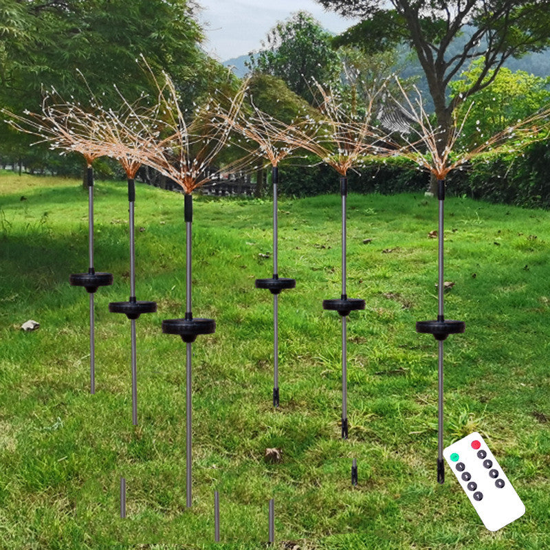 Solar-powered garden lights with multiple LED strands, resembling sparklers, are staked into a grassy lawn. A remote control is visible in the foreground.