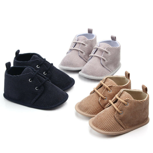 Three pairs of baby shoes are displayed: one black, one beige, and one brown. All shoes have a ribbed texture and lace-up design, arranged on a plain white background.