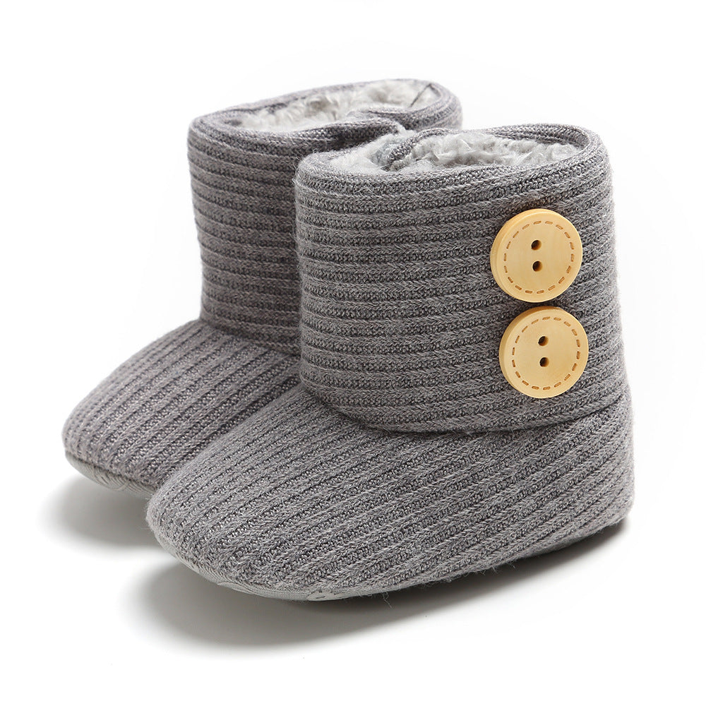 Gray knitted baby booties with cozy lining and ribbed texture. They feature two large wooden buttons on the side, adding a cute, functional detail.