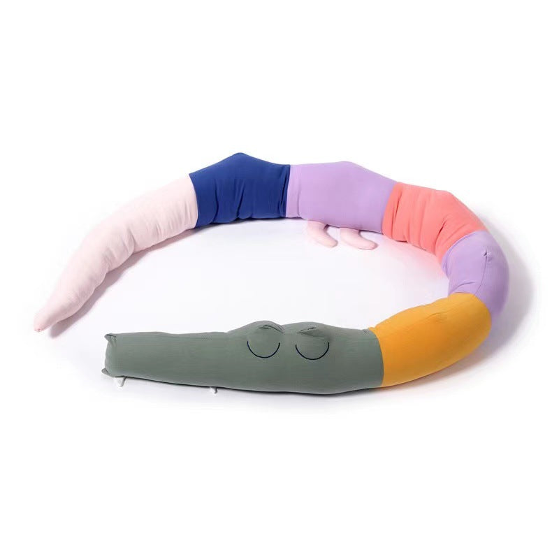 A colorful, segmented caterpillar pillow with closed eyes. Its body features pastel shades of pink, blue, purple, orange, and green, coiled in a semi-circle on a white background.