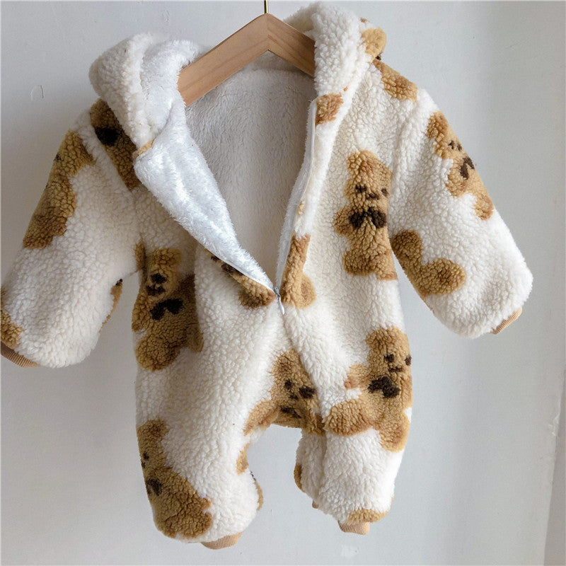 A fluffy infant onesie with a teddy bear pattern in beige and brown. The hooded outfit is hanging on a wooden hanger against a plain wall, showcasing its cozy fabric.