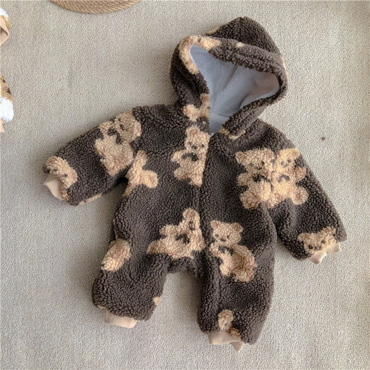 A fluffy, brown baby onesie with a hood, adorned with beige teddy bear patterns. The outfit is laid flat on a light beige surface, showcasing its cozy texture.