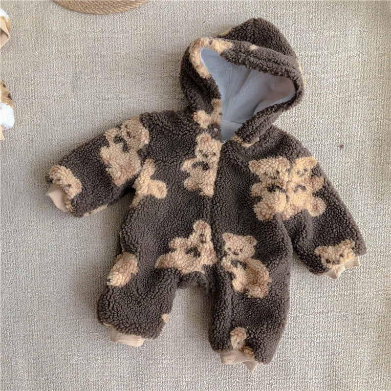A fluffy brown baby onesie with a hood, featuring a tan teddy bear pattern, lies on a light textured surface.