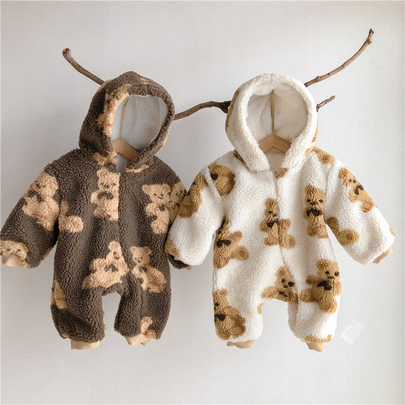 Two hooded baby onesies hang on wooden hangers. One is brown with teddy bear patterns, and the other is white with similar bear designs. Both are cozy and fluffy.