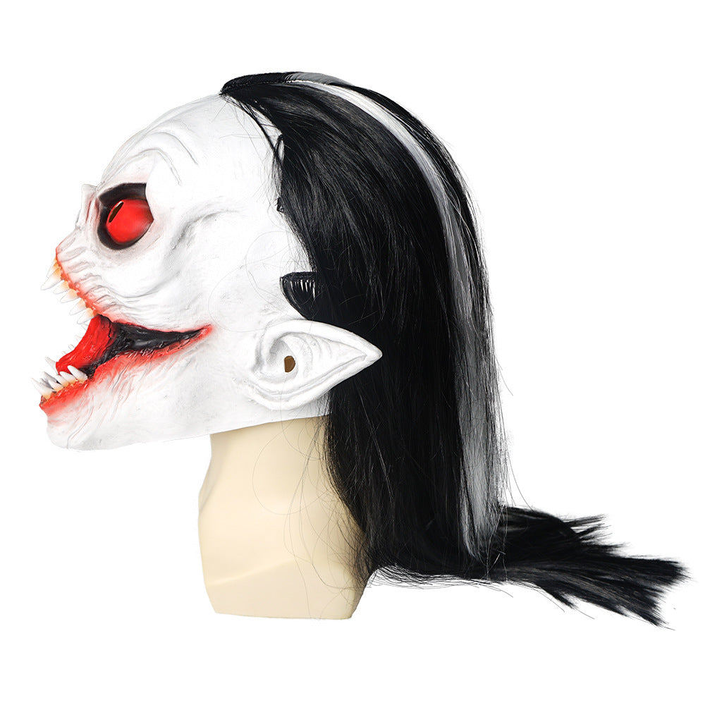 Side view of a Halloween mask featuring a white, demonic face with exaggerated red eyes and mouth, sharp teeth, pointed ears, and long black hair with a gray streak.