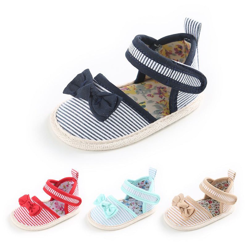 Striped baby shoes with floral insole and bow accent. Main shoe is navy and white; smaller versions in red, light blue, and beige displayed below.