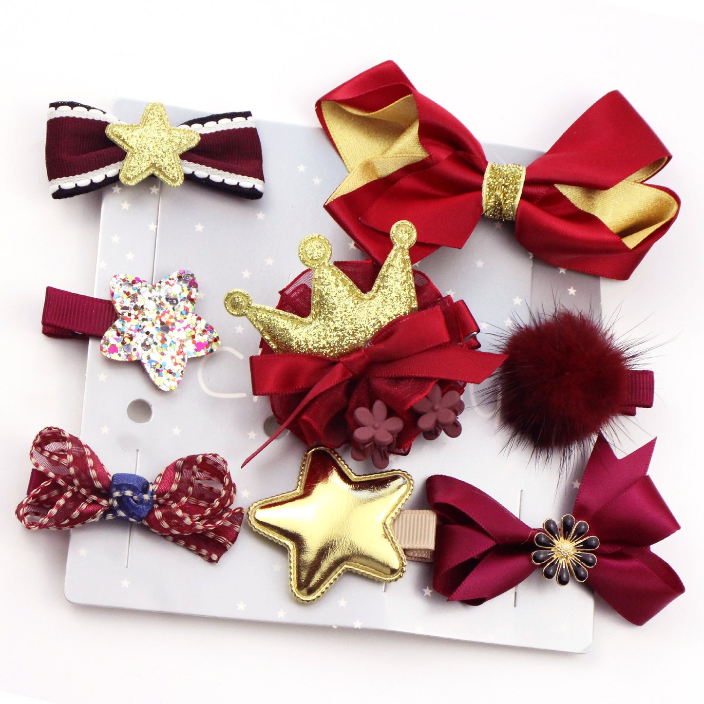 A collection of decorative hair clips on a card, featuring red bows, gold and glittery stars, a fluffy pom-pom, a crown, and flower embellishments.