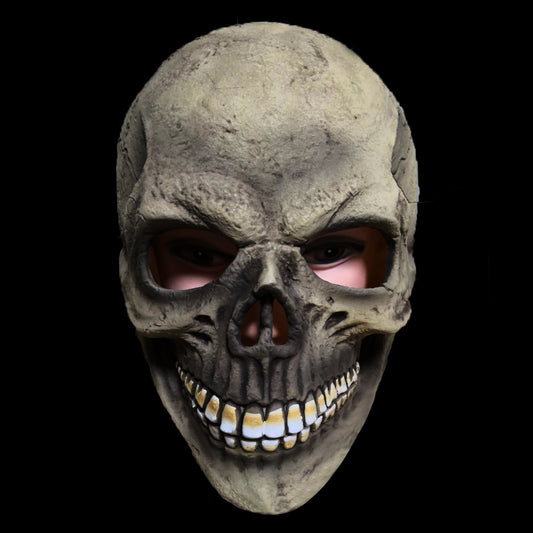 Close-up of a realistic skull mask with hollow eye sockets, worn by a person. The mask features detailed textures, an exaggerated smile, and a dark background.