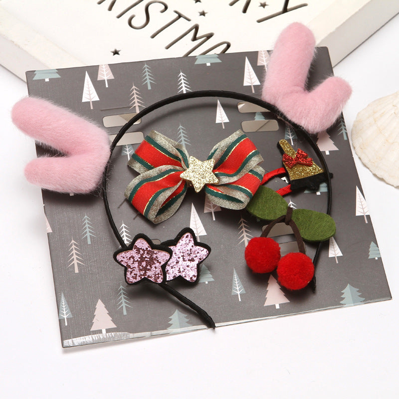 Pink plush antlers, a striped bow with a gold star, red pom-pom cherries, glittery star clips, and a Christmas mitten hair accessory on a gray tree-patterned card.