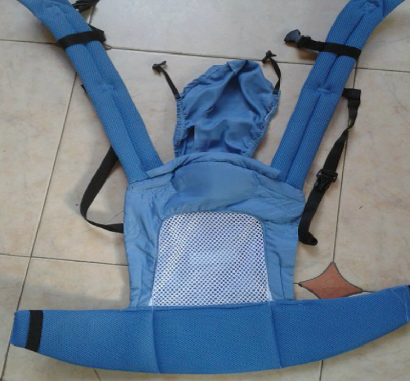 Blue ergonomic baby carrier with mesh front panel, adjustable padded straps, and a hood, lying flat on a tiled floor.