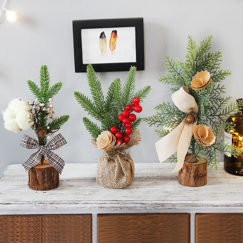 Three mini faux Christmas trees on a wooden table. Each tree is decorated with different ornaments: cotton balls, red berries, and beige flowers, and placed in rustic log bases.
