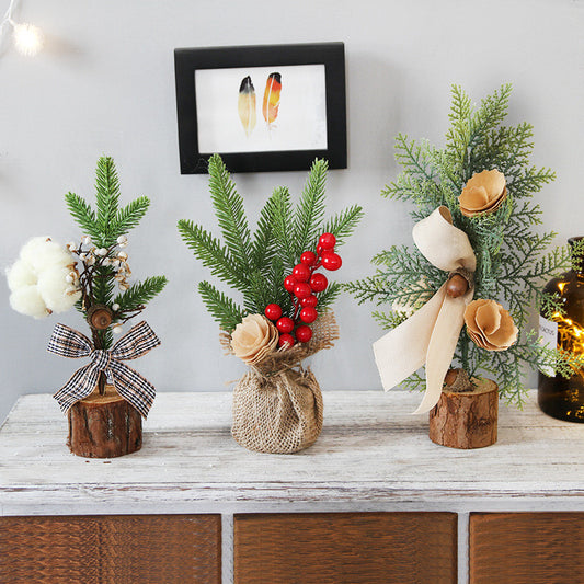 Three mini faux Christmas trees on a wooden table. Each tree is decorated with different ornaments: cotton balls, red berries, and beige flowers, and placed in rustic log bases.