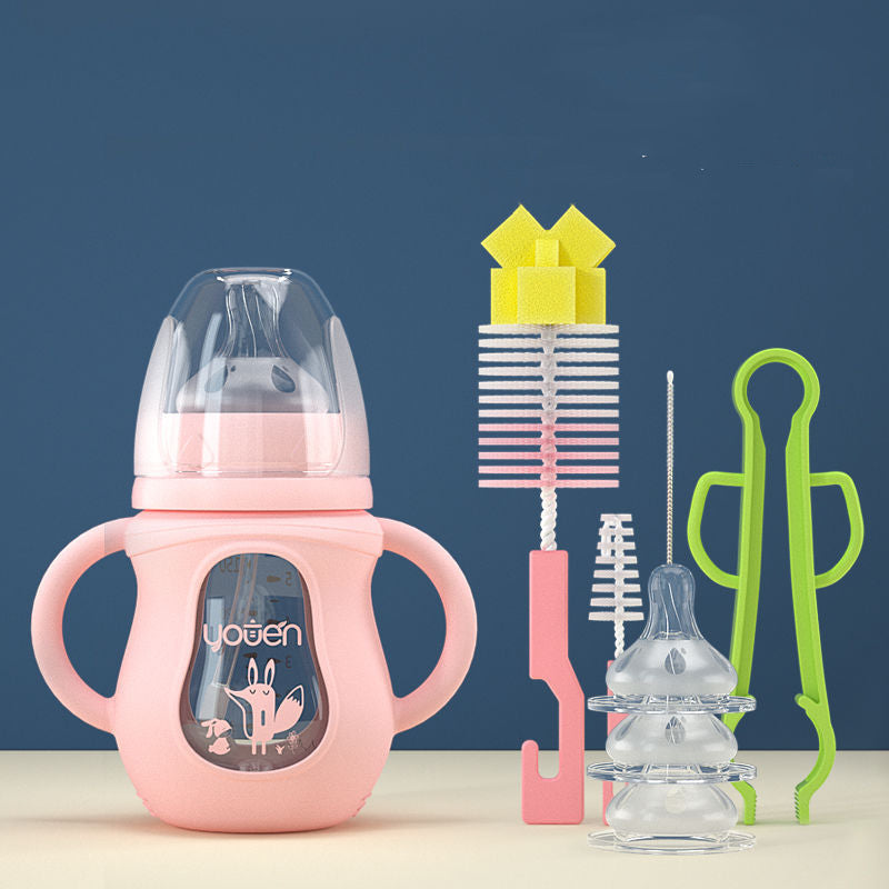 Pink baby bottle with handles, cleaning brushes, and clear bottle nipples. Additional cleaning tools include a yellow sponge brush, a green tong, and small brushes, set against a dark background.