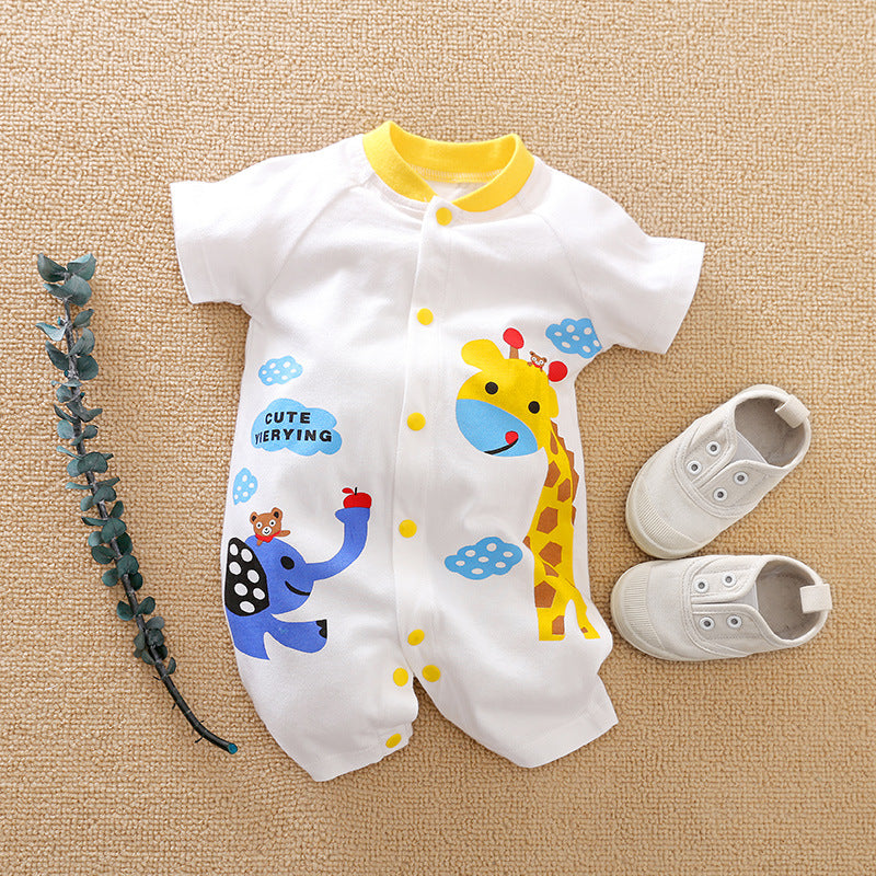White baby romper with colorful giraffe and elephant print, yellow accents, and small buttons, alongside a pair of white baby shoes and a sprig of green leaves on a beige background.