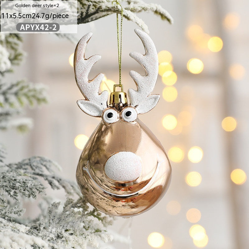 Gold reindeer-shaped Christmas ornament with white antlers and facial features, hanging on a frosted tree branch. Warm, glowing lights are softly blurred in the background.