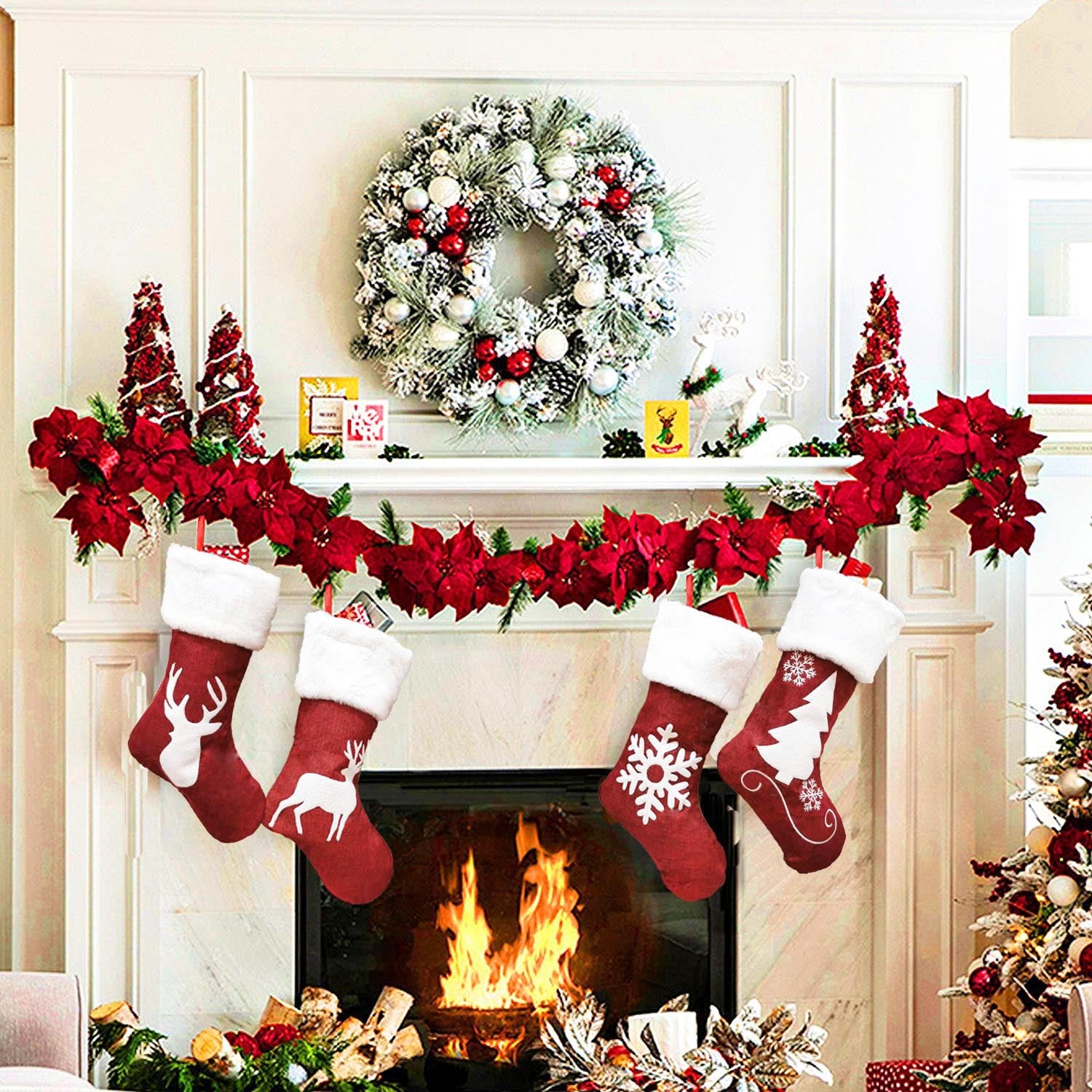 Festive fireplace with a roaring fire, decorated with a snowy wreath, red floral garland, and four hanging red stockings featuring deer, snowflake, and tree designs.