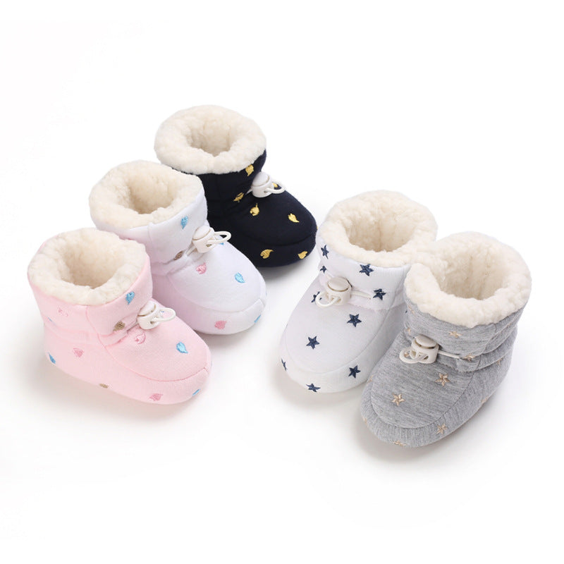 Four pairs of baby booties with fur lining in pink, white, black, and gray. Each has a unique star or heart pattern, and they feature a toggle closure.