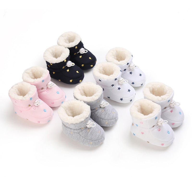 A variety of soft baby booties in pink, black, gray, and white, each with unique patterns like stars and hearts, lined with fleece, arranged in rows on a white background.