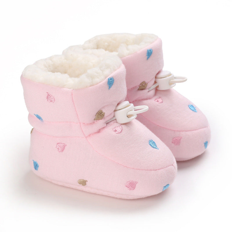 Soft pink baby booties with a fluffy white lining, decorated with small embroidered blue, pink, and brown teardrop shapes, featuring a white toggle closure.