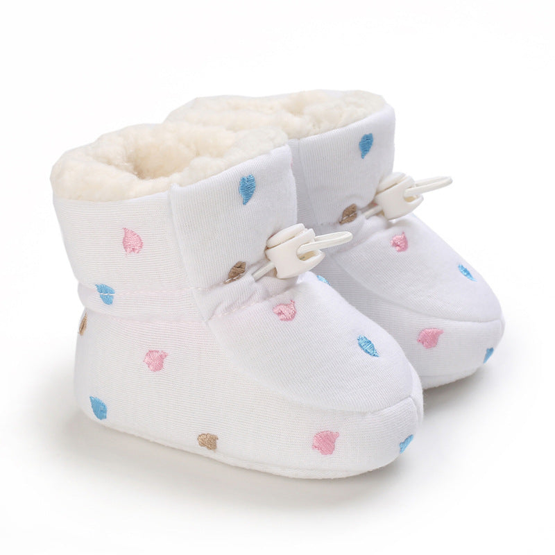 White baby booties with colorful embroidered leaves in pink, blue, and brown. They are lined with plush cream material and have secure white fasteners.