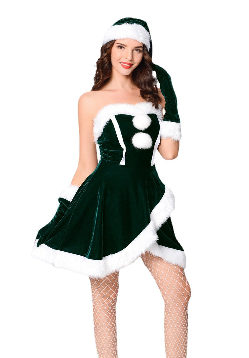 Woman in a festive green velvet dress with white fur trim, matching gloves and hat, posing with a smile against a plain background. She wears fishnet stockings.