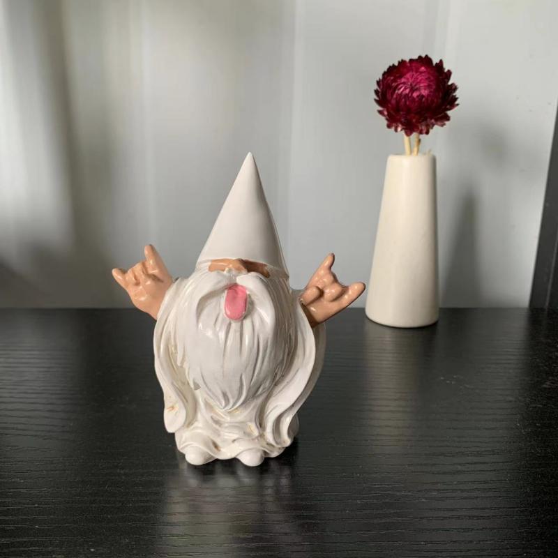 Ceramic gnome with a tall hat, white beard, and outstretched arms making rock and roll hand gestures. It stands on a dark surface, next to a white vase with a red flower.