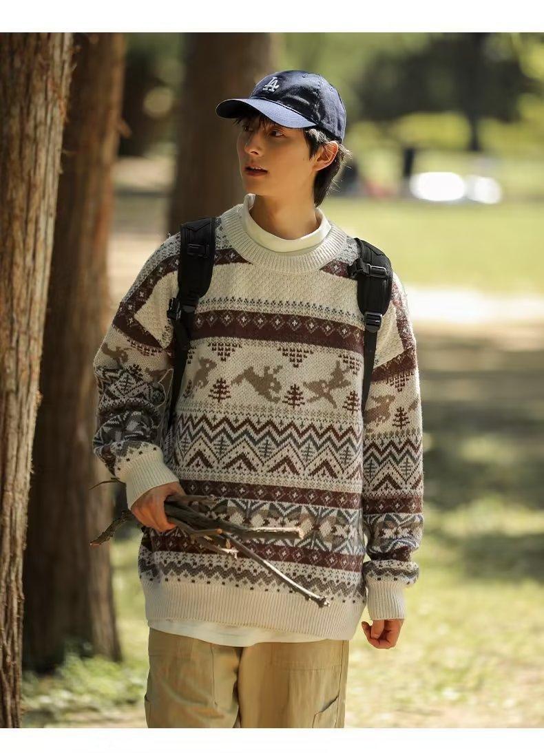 Person outdoors wearing a patterned sweater, beige cargo pants, and a dark cap. They carry a bundle of sticks and have a backpack, standing in a sunlit park.