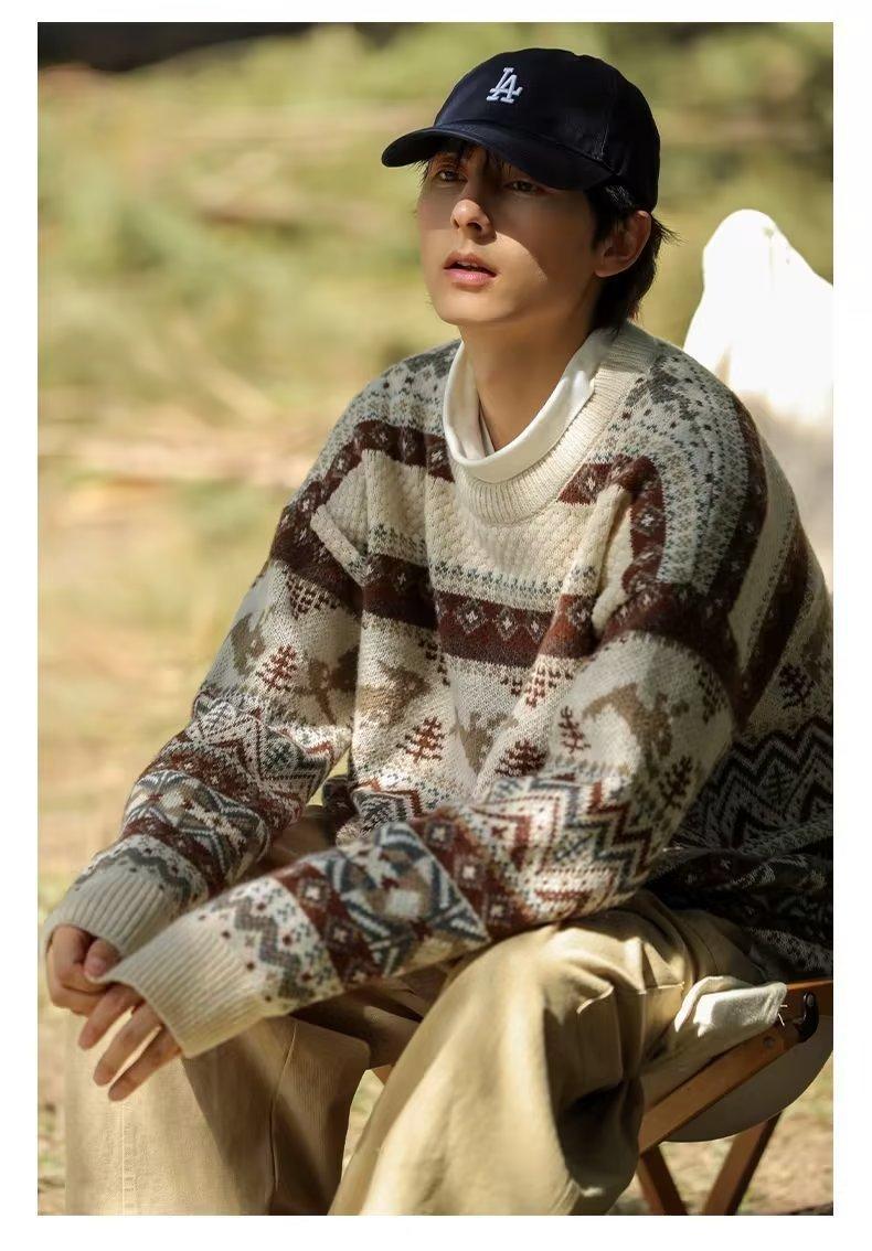 A person sits outdoors wearing a patterned sweater and a black cap, surrounded by a blurred green background, suggesting a serene, natural setting.