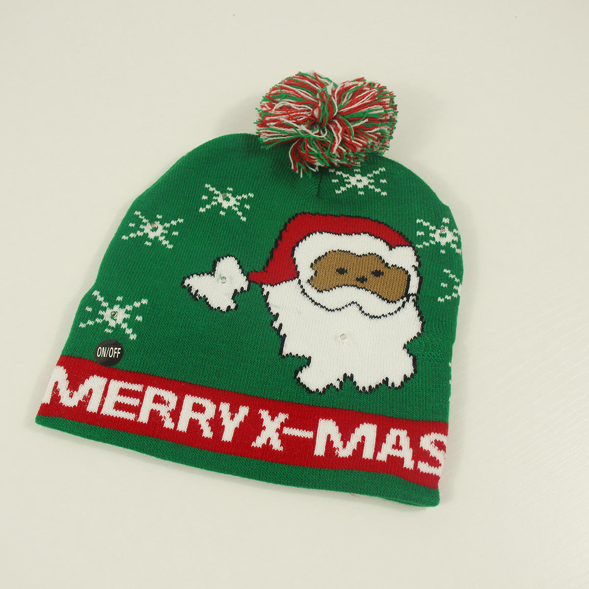 Green holiday beanie with a red and white pom-pom, featuring a Santa Claus design and snowflakes. "MERRY X-MAS" is written in bold red and white on the brim.