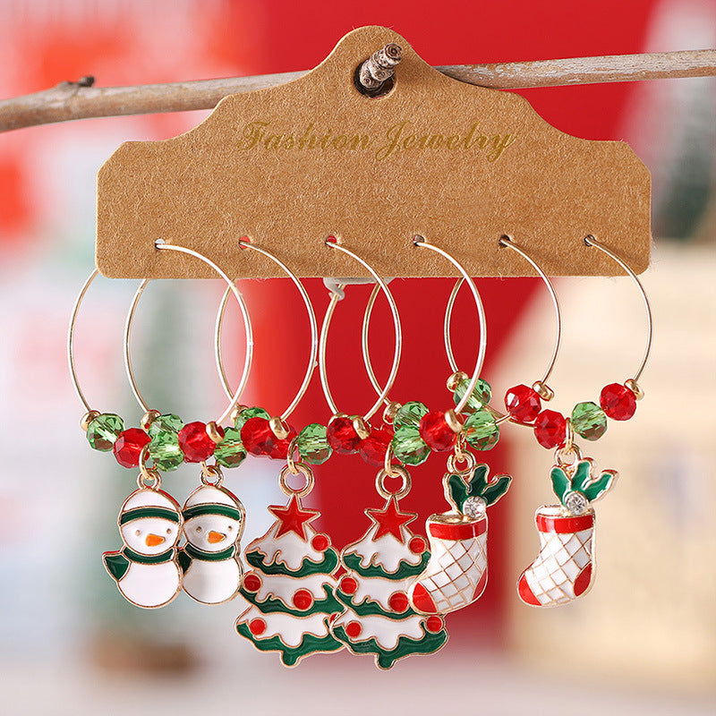 Festive Christmas wine glass charms with holiday designs: snowmen, Christmas trees, and stockings, adorned with red and green beads on a display card labeled "Fashion Jewelry."