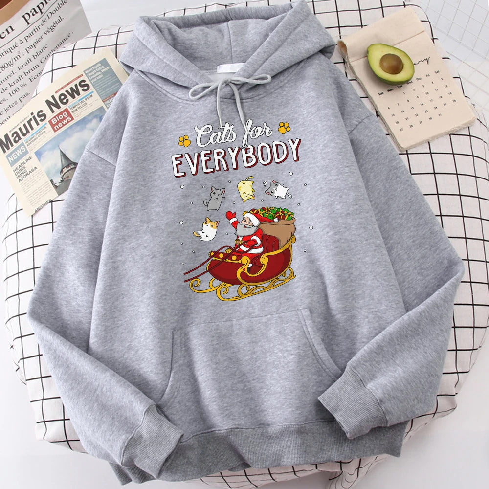 Gray hoodie with "Cats for Everybody" text and Santa cartoon in a sleigh with cats. Nearby are a newspaper, an open planner, and half an avocado on a checkered surface.