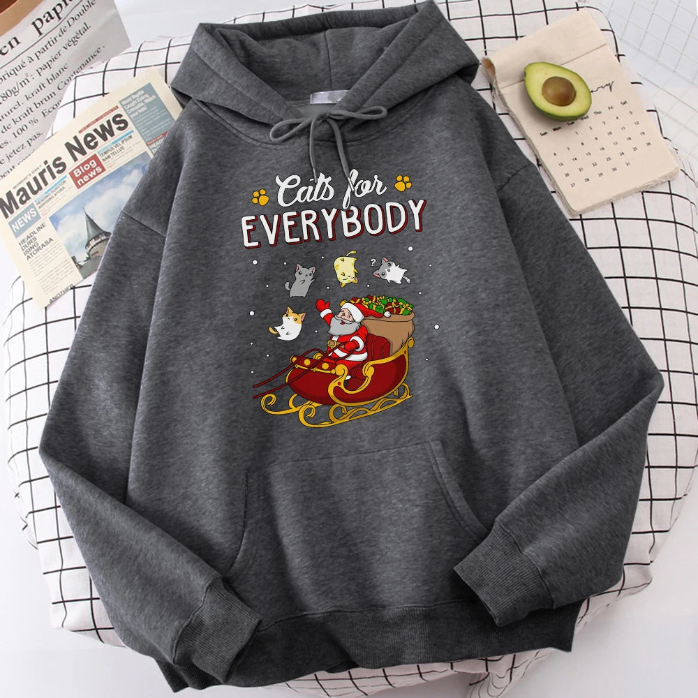 Gray hoodie with "Cats for Everybody" text and Santa in a sleigh with cats, set on a checkered surface. Nearby are an avocado half, newspaper, and a small calendar.